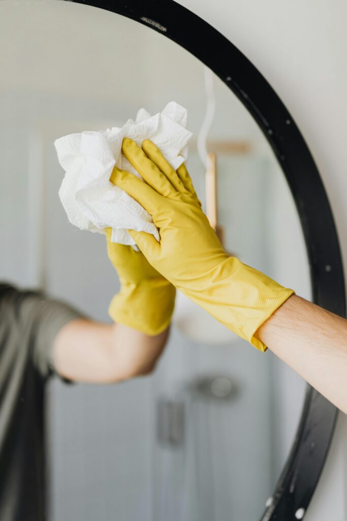 Close-up of a person cleaning a mirror with yellow gloves, focusing on hygiene and sanitation.