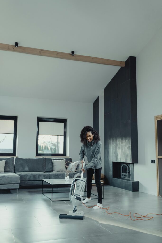 Black woman using vacuum in contemporary living room. Clean and modern setting.